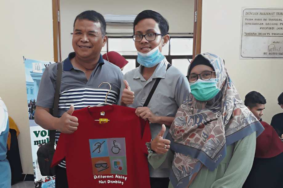 Perwakilan dari Komunitas Mata Hati sedang berfoto dengan memegang baju berwarna merah.